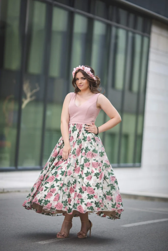 A Caucasian woman in a pink dress and hairband standing confidently in front of a modern building."