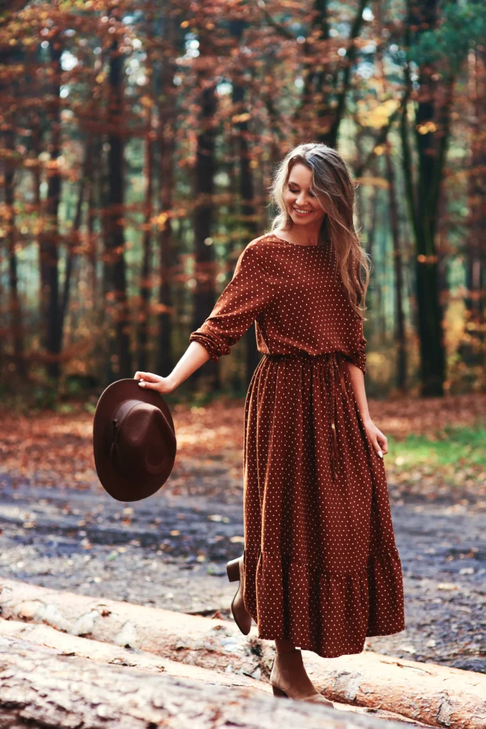 Young woman walking peacefully in the woods while holding her hat, surrounded by green trees